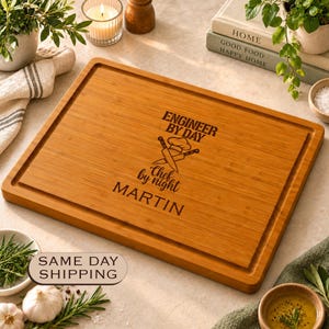 May include: A rectangular bamboo cutting board with a juice groove along the perimeter. The center features an engraved design with a chef hat, crossed knives, and the text: ENGINEER BY DAY, Chef by night, MARTIN.