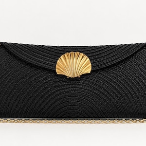 Op de afbeelding: Een zwarte gevlochten clutch met een gebogen flap en een goudkleurige metalen sluiting in de vorm van een schelp. De tas is voorzien van een afneembare goudkleurige schouderketting met ronde schakels, wat zorgt voor een gestructureerd accessoire.