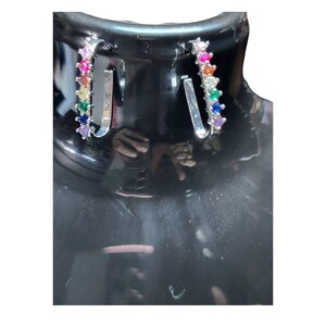 May include: A pair of silver-toned U-shaped hoop earrings featuring a row of small, round, multi-colored gemstones in a rainbow gradient pattern, including red, orange, yellow, green, blue, and purple stones set along the front edge.