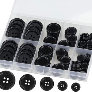 May include: A clear plastic storage container with multiple compartments filled with various sizes of round black buttons, each featuring four holes in the center. Five individual black buttons of different sizes are arranged in a row below the box.