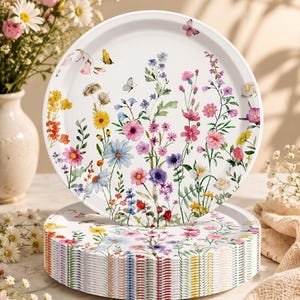 May include: A stack of round white paper plates featuring a colorful botanical print of various wildflowers in shades of pink, blue, yellow, and purple, accented with small butterflies scattered across the surface of each plate.