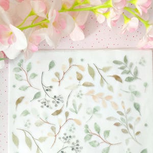 Op de afbeelding: Een rechthoekig vel met doorschijnende stickers met een herhalend patroon van botanische illustraties in aquarel-stijl, waaronder diverse groene en bruine bladeren, delicate takjes en kleine besjes verspreid over een witte achtergrond.