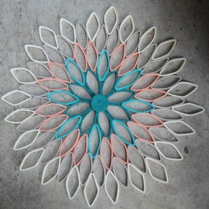 May include: A paper flower wall decor made from rolled paper, featuring a circular design with overlapping petals in shades of white, peach, teal, and blue.