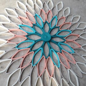 May include: A large paper flower wall decor made from rolled paper, with a teal center and layers of peach and white paper petals.