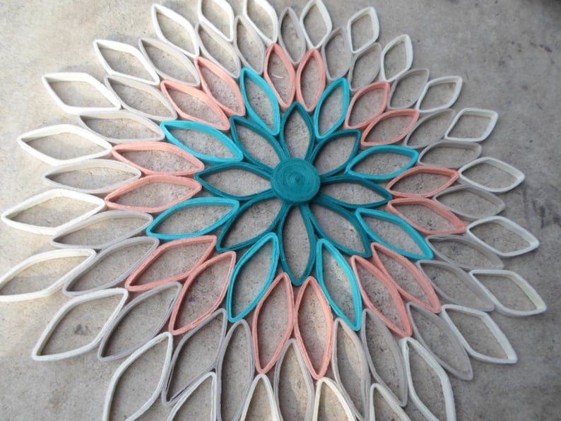May include: A large paper flower wall decor made from rolled paper, with a teal center and layers of peach and white paper petals.