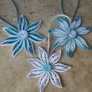 May include: Three paper quilled ornaments in the shape of flowers. Two are teal blue with white centers and one is white with a teal blue center.