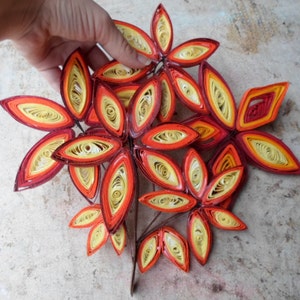 May include: A cluster of paper quilled leaves in shades of red, orange, and yellow, arranged in a flower-like shape.