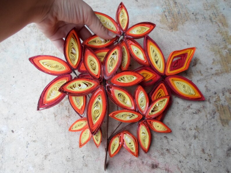 May include: A cluster of paper quilled leaves in shades of red, orange, and yellow, arranged in a flower-like shape.