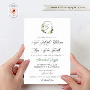 May include: A white wedding invitation card featuring a floral wreath crest with the initials ZL, printed with black text announcing the marriage of Zoe Gabrielle Williams and Liam John Finkle in Savannah, Georgia, on Saturday, May 23, 2026.