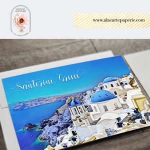 Pode incluir: Uma pintura em aquarela de edif&iacute;cios brancos com c&uacute;pulas azuis em Santorini, Gr&eacute;cia. O texto "Santorini, Gr&eacute;cia" est&aacute; escrito em caligrafia branca sobre um fundo azul.