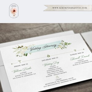 May include: A white wedding itinerary card featuring a light blue banner with the text Wedding Itinerary, decorated with floral illustrations. The card lists events for Friday, Saturday, and Sunday in Savannah, GA, with small icons for each event.