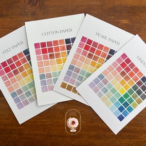 May include: Four white rectangular paper sample sheets labeled Felt Paper, Cotton Paper, Pearl Paper, and Linen Paper. Each sheet features a grid of small, multi-colored watercolor squares in various shades of red, orange, yellow, green, blue, and purple.