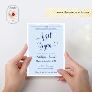 Pode incluir: Convite de casamento com fundo azul aquarela. O convite anuncia o casamento de April e Bryan na ilha de Santorini, Gr&eacute;cia, em 20 de maio de 2025 &agrave;s 17h. O convite inclui o texto "Le Ciel Santorini" e "Seguido de boa comida, vinho e dan&ccedil;a."