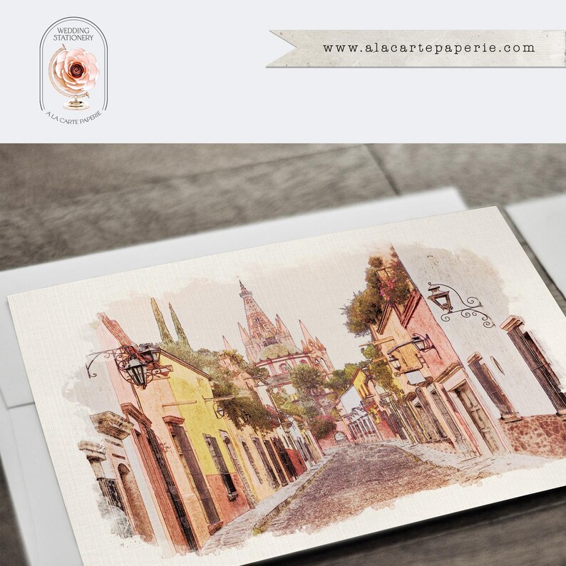 Puede incluir: Papeler&iacute;a de boda estilo acuarela con una escena callejera con edificios coloridos y un campanario. La papeler&iacute;a incluye el texto "Wedding Stationery" y la direcci&oacute;n del sitio web "www.alacartepaperie.com". El dise&ntilde;o est&aacute; sobre papel texturizado.