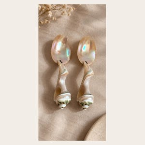 Peut inclure: Une paire de cuillères fabriquées à partir de coquillages en nacre irisée. Chaque cuillère présente un bol lisse de forme ovale avec un éclat nacré et un manche en coquillage naturel en spirale passant du beige crème à une base vert foncé.