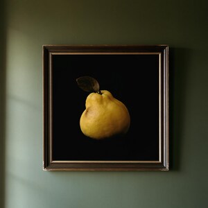 May include: A square framed wall art piece featuring a single yellow quince fruit with a dark brown leaf against a solid black background. The artwork is enclosed in a dark brown wooden frame with a thin gold inner border, displaying a still life.