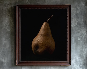 May include: A framed wall art piece featuring a single brown, textured pear centered against a solid black background. The artwork is enclosed in a dark brown wooden frame with a beaded inner edge, creating a stark contrast between the fruit and frame.