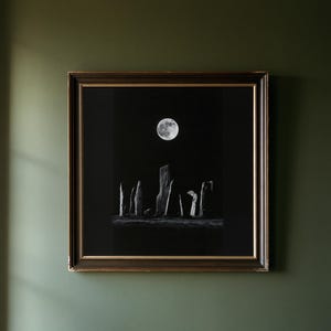 May include: A square framed wall art piece featuring a black and white photograph of a group of tall, upright standing stones arranged in a field under a bright, full moon set against a deep black night sky, enclosed in a dark brown frame.
