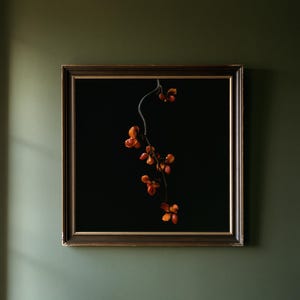 May include: A square framed wall art piece featuring a dark brown wooden frame with gold inner detailing. The artwork displays a single thin, dark branch with small, vibrant orange-red seed pods centered against a solid black background.