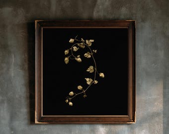 Puede incluir: Una pieza de arte mural cuadrada con un marco de madera marrón oscuro y un borde interior con cuentas. En el interior, un fondo negro muestra una sola enredadera de lúpulo dorada y delicada con varios conos texturizados y tallos finos.