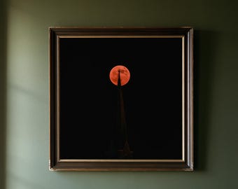 May include: A square framed wall art piece featuring a dark night sky with a large, vibrant orange full moon positioned directly behind the pointed spire of a church steeple, which is topped with a small cross silhouette against the darkness.