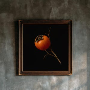 May include: A square framed wall art piece featuring a single bright orange persimmon fruit attached to a thin, bare brown twig. The fruit and branch are centered against a solid black background, enclosed in a dark brown wooden frame.