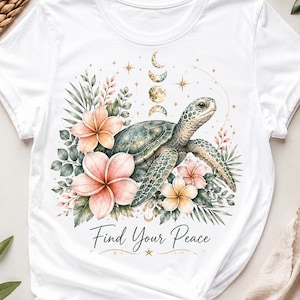 May include: A white t-shirt featuring a graphic print of a sea turtle surrounded by pink and peach tropical flowers, green foliage, and a vertical moon phase cycle. The text "Find Your Peace" is printed in black script below the illustration.