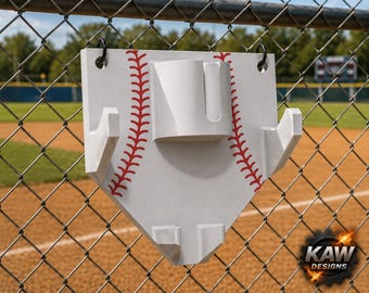 May include: A white home plate-shaped wall mount featuring red baseball stitching graphics. The mount includes two side hooks, a central cylindrical holder with a vertical cutout, and two bottom supports. Two black metal rings are attached at the top.