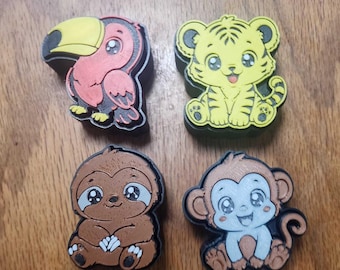 May include: Four decorative charms featuring cartoon animal designs: a pink and black toucan, a yellow tiger with black stripes, a brown sloth, and a brown and white monkey. Each charm has a black base and a detailed, colorful top surface.