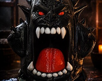 May include: A black, horned creature sculpture with a wide-open mouth, prominent white fangs, and a textured red tongue. The figure features glowing red eyes, sharp spikes along its head and sides, and a glossy finish on its dark, detailed surface.