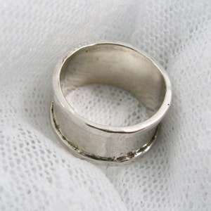 May include: A silver ring with a wide band. The ring is smooth and polished.