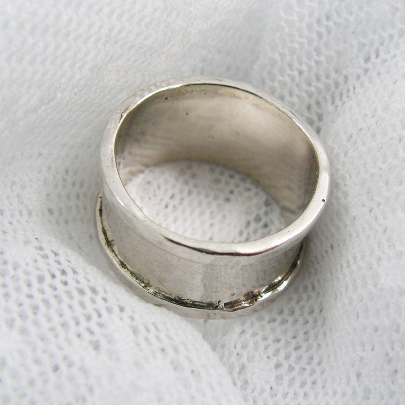 May include: A silver ring with a wide band. The ring is smooth and polished.