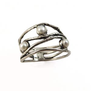 May include: A silver-toned ring with three round, white pearls. The ring has an open design with multiple bands and a textured, organic appearance. The pearls are evenly spaced across the top of the ring.