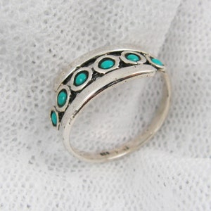 K&ouml;nnte beinhalten: Ein Silberring mit einem Band, das eine Reihe von t&uuml;rkisfarbenen Steinen in einzelnen Fassungen aufweist. Der Ring hat ein leicht gebogenes Design und eine polierte Oberfl&auml;che, die die leuchtend blau-gr&uuml;nen Steine zur Geltung bringt.
