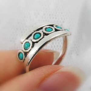 K&ouml;nnte beinhalten: Ein silberner Ring mit t&uuml;rkisfarbenen Steinen in einem geschwungenen Design. Der Ring hat eine polierte Oberfl&auml;che und einen einzigartigen, k&uuml;nstlerischen Stil. Der Ring hat die Gr&ouml;&szlig;e 54 (DE), ca. 1,73 cm Durchmesser, und ist perfekt, um Farbe zu verleihen.