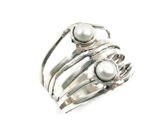May include: A silver ring with a unique design, featuring multiple bands and two prominent, round, white pearls. The ring has a textured, handcrafted appearance, with a modern and artistic aesthetic.