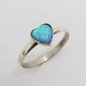 May include: A silver ring featuring a heart-shaped opal gemstone. The opal displays a vibrant mix of blue and green hues. The ring has a simple, elegant design, with a smooth, polished band.