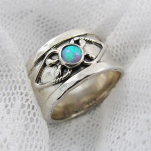 May include: A silver ring with a blue opal gemstone set in a decorative design. The ring is wide and has a textured surface.