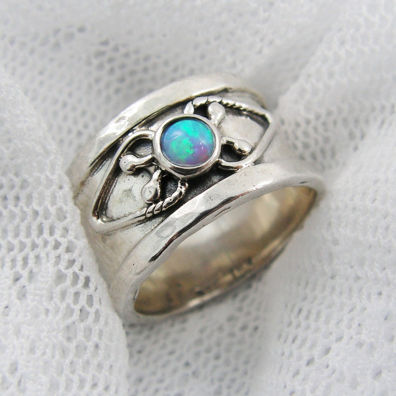 May include: A silver ring with a blue opal gemstone set in a decorative design. The ring is wide and has a textured surface.