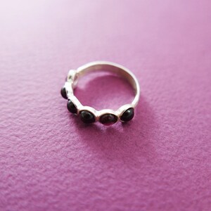 Pu&ograve; includere: Un anello d'argento con una serie di pietre scure di forma ovale. L'anello &egrave; posto su una superficie viola, con le pietre che mostrano un colore intenso e ricco. Il design dell'anello &egrave; semplice ed elegante.