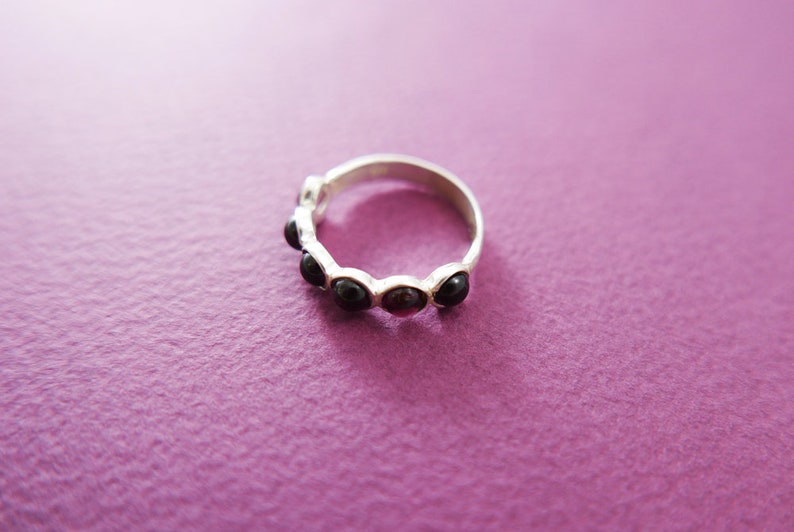 Pu&ograve; includere: Un anello d'argento con una serie di pietre scure di forma ovale. L'anello &egrave; posto su una superficie viola, con le pietre che mostrano un colore intenso e ricco. Il design dell'anello &egrave; semplice ed elegante.