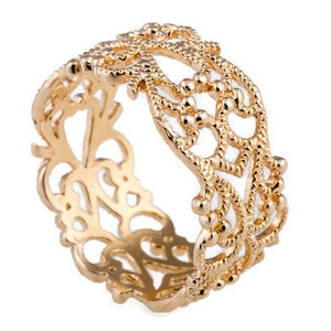 May include: A gold-colored ring with an intricate openwork design. The ring features a repeating pattern of floral and geometric shapes, with small beaded accents. The ring is made of a shiny, polished metal.