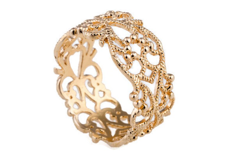 May include: A gold-colored ring with an intricate openwork design. The ring features a repeating pattern of floral and geometric shapes, with small beaded accents. The ring is made of a shiny, polished metal.