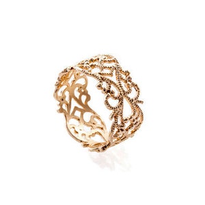 May include: A gold-colored ring with an intricate openwork design. The ring features a continuous pattern of interwoven shapes and delicate details, creating a lace-like appearance. The ring is set against a white background.