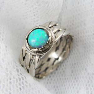 Puede incluir: Anillo de plata con una piedra de &oacute;palo iridiscente. El anillo presenta un dise&ntilde;o tejido alrededor de la banda y el engaste. El &oacute;palo muestra tonos azules y verdes. Dise&ntilde;o detallado.