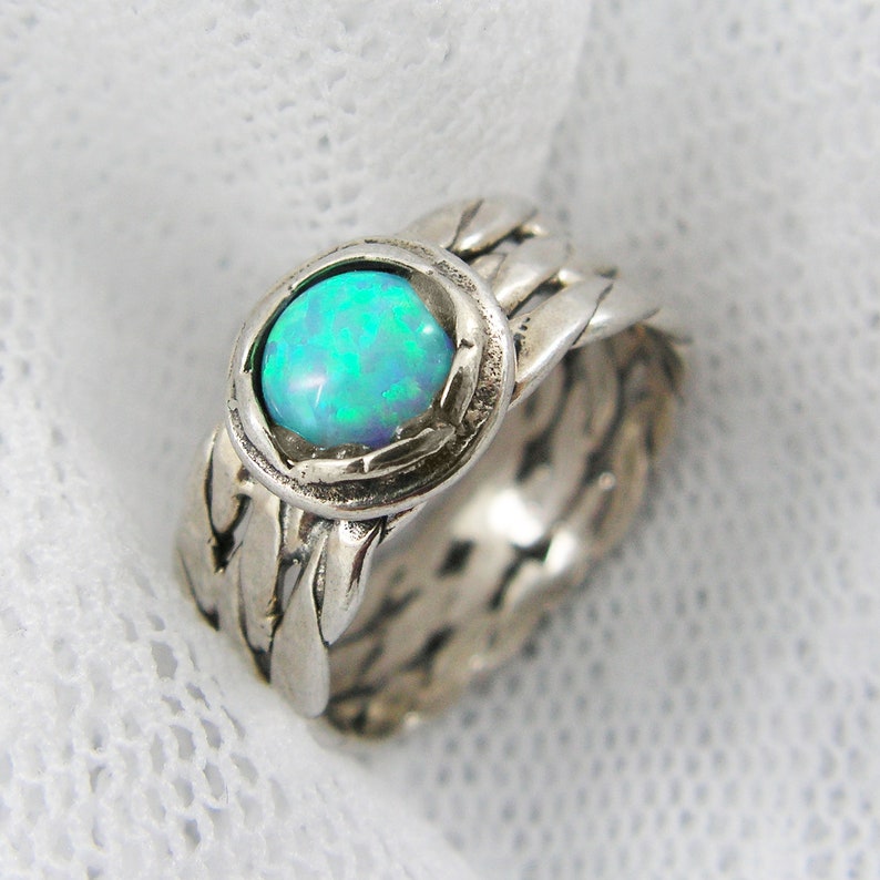 Puede incluir: Anillo de plata con una piedra de &oacute;palo iridiscente. El anillo presenta un dise&ntilde;o tejido alrededor de la banda y el engaste. El &oacute;palo muestra tonos azules y verdes. Dise&ntilde;o detallado.