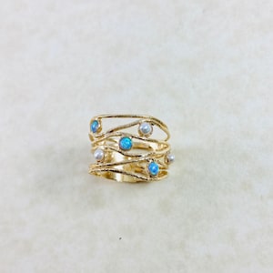Può includere: Un anello d'oro con un design delicato e ondulato con opali blu e perle bianche.