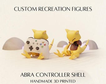 May include: Two yellow Abra figures, one holding a white game controller and one sitting, with text reading CUSTOM RECREATION FIGURES, ABRA CONTROLLER SHELL, and HANDMADE 3D PRINTED. The figures have pointed ears, brown chest markings, and tails.