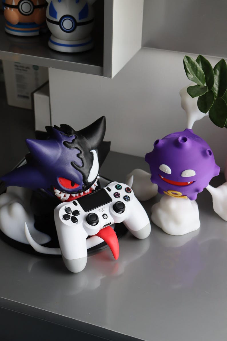 May include: A purple and black character figure with sharp teeth and red eyes holding a white game controller with a long red tongue. Beside it stands a smaller purple spherical character with white eyes and a yellow ring, surrounded by white smoke.