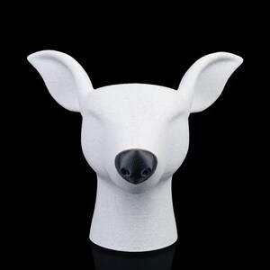 May include: A white deer head sculpture with a textured surface and a smooth black nose. The animal head is depicted from the front, featuring large pointed ears and a clean, solid white finish that contrasts with the dark, detailed nose.